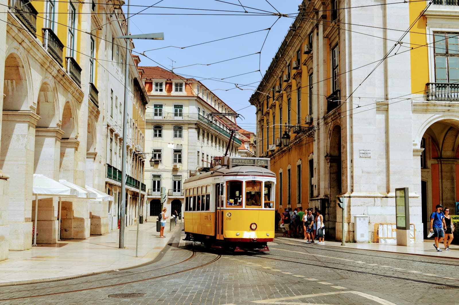 A yellow tram on a curved street in Lisbon, with overhead wires and stone buildings